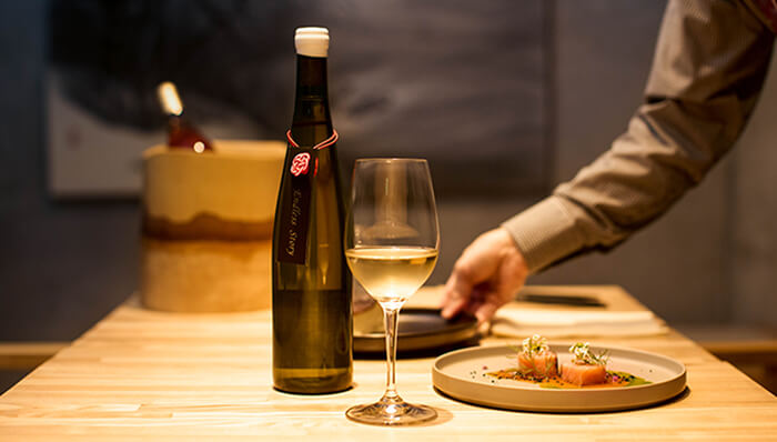 グラスに注がれた白ワインと細長いボトルが木のテーブルに置かれている