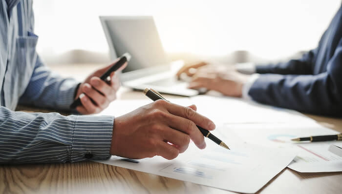 スーツ姿の人物が資料にペンを走らせ、スマートフォンを手にする様子