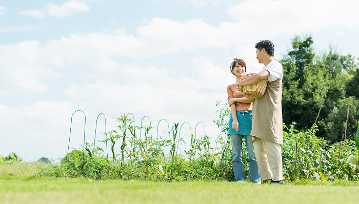 晴天の畑で収穫かごを持った男女が笑顔で立つ自然豊かな風景
